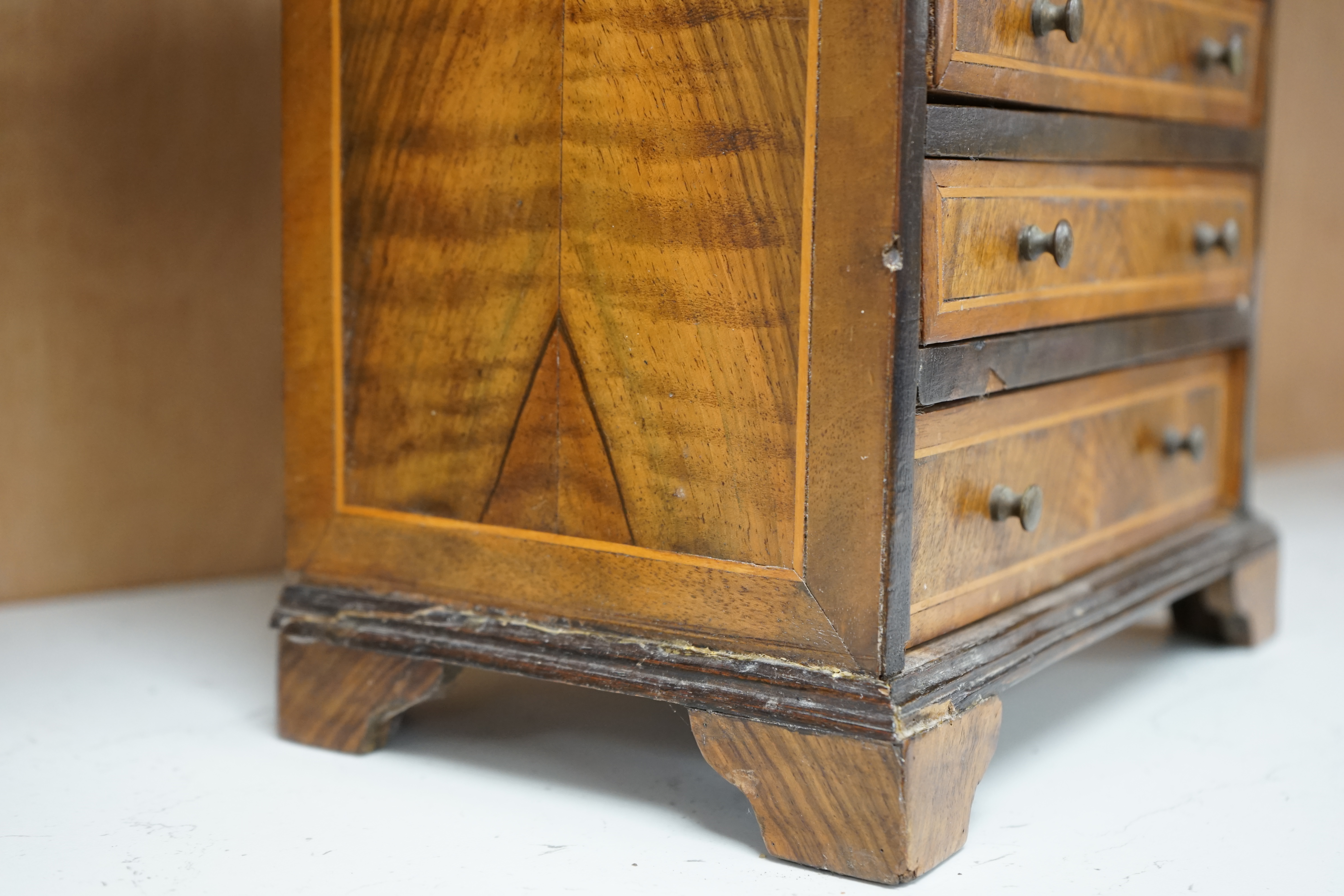 A miniature three long and two short inlaid chest of drawers, 21.5cm high x 23.5cm wide. Condition - poor to fair